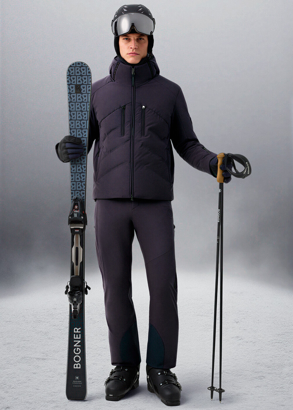 The female model is wearing a beige ski outfit, a white ski helmet, and is holding skis.