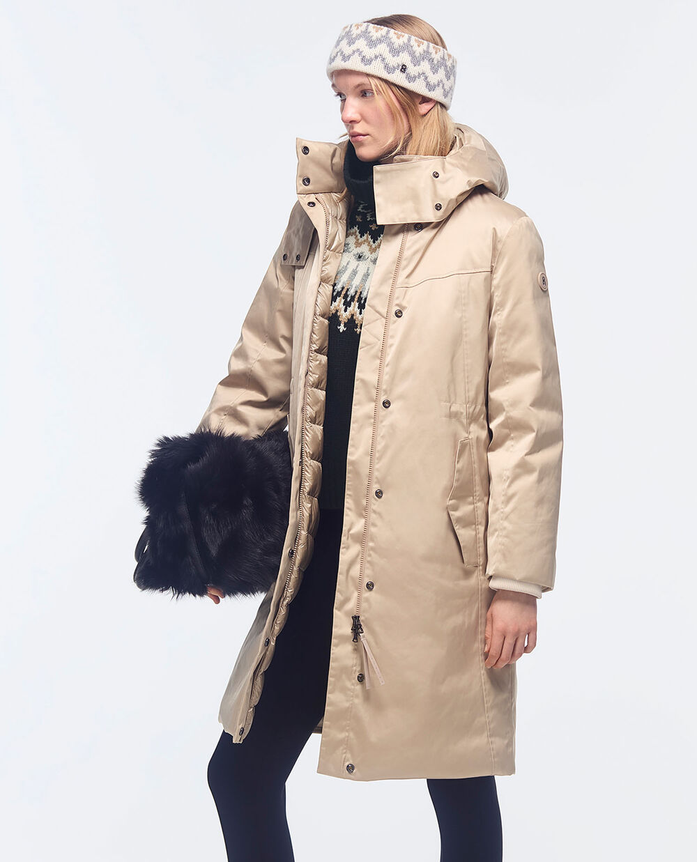 The model is wearing a down jacket in beige, a black norwegian knit, black pants and a furry bag.