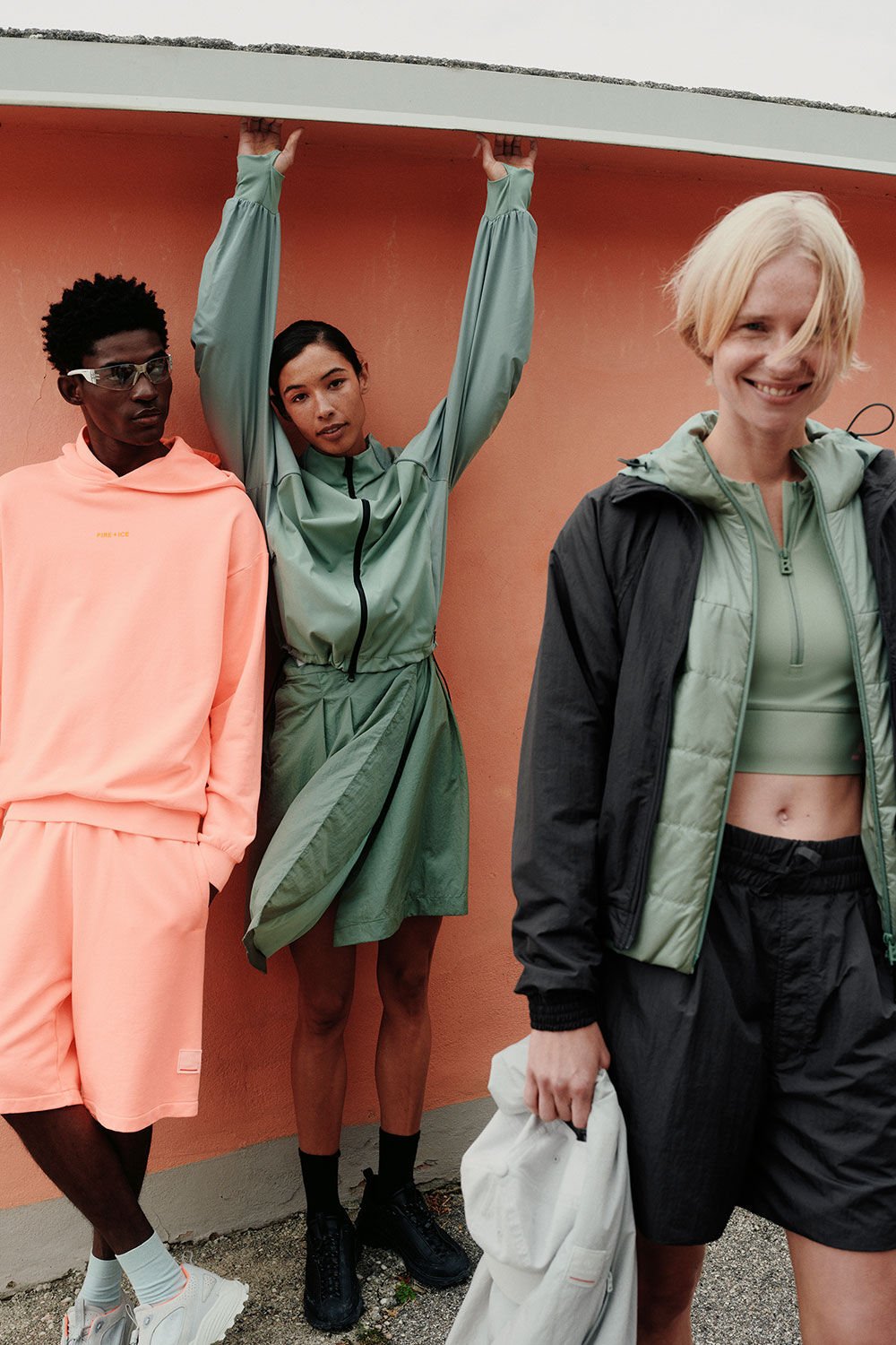 A group of three models, two female, one male, in FIRE+ICE looks. There is an apricot-colored wall behind them.