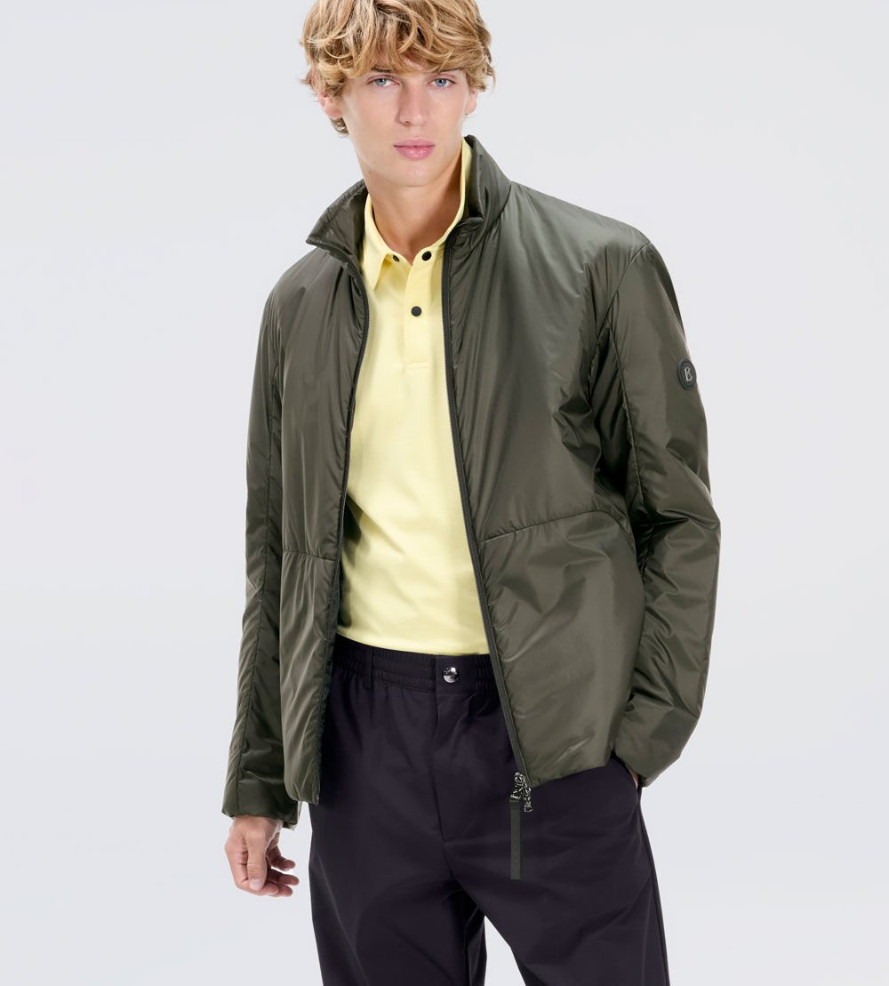 The male model is wearing a pale yellow polo shirt, a green padded blouson and dark trousers. 