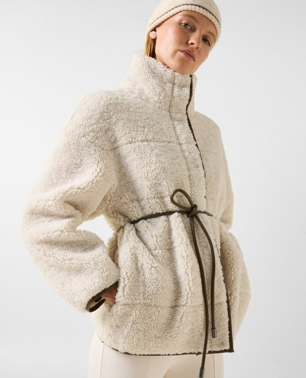 The model is wearing the Kimberly teddy fur jacket with faux leather piping and a narrow tie.
