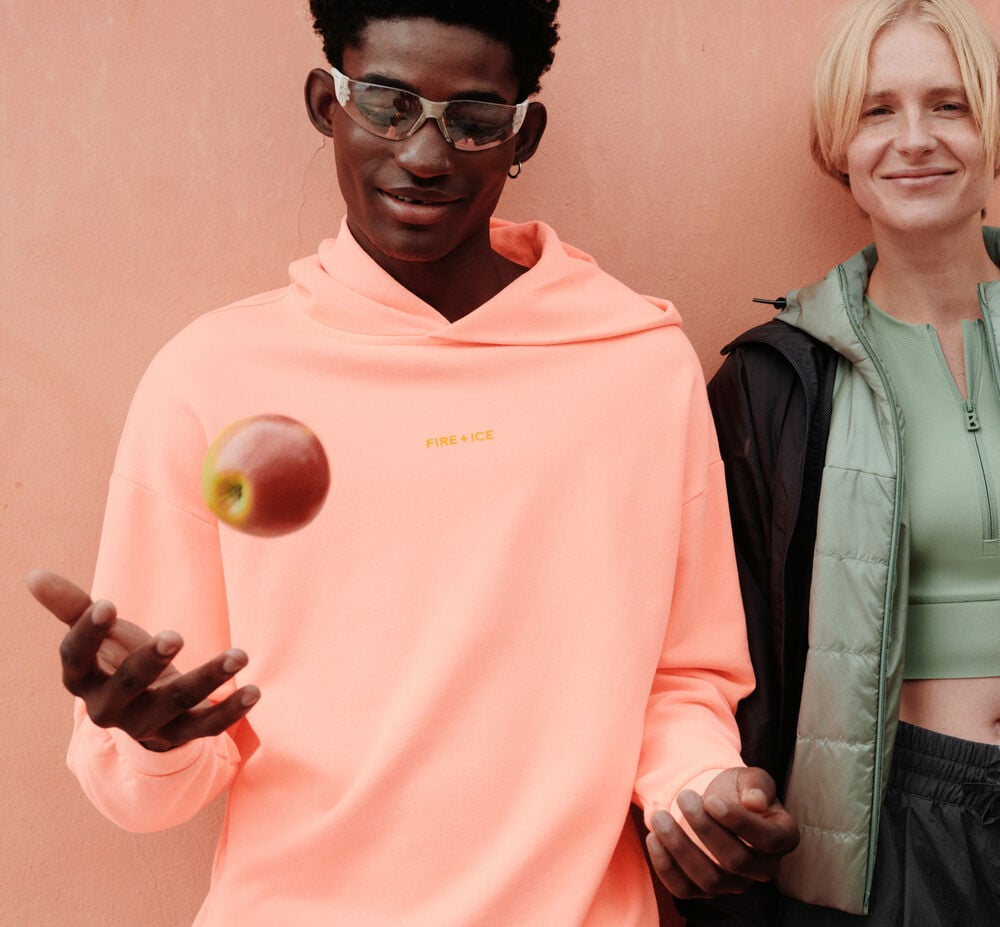 The male model is wearing an apricot hoodie with a logo print and sunglasses.