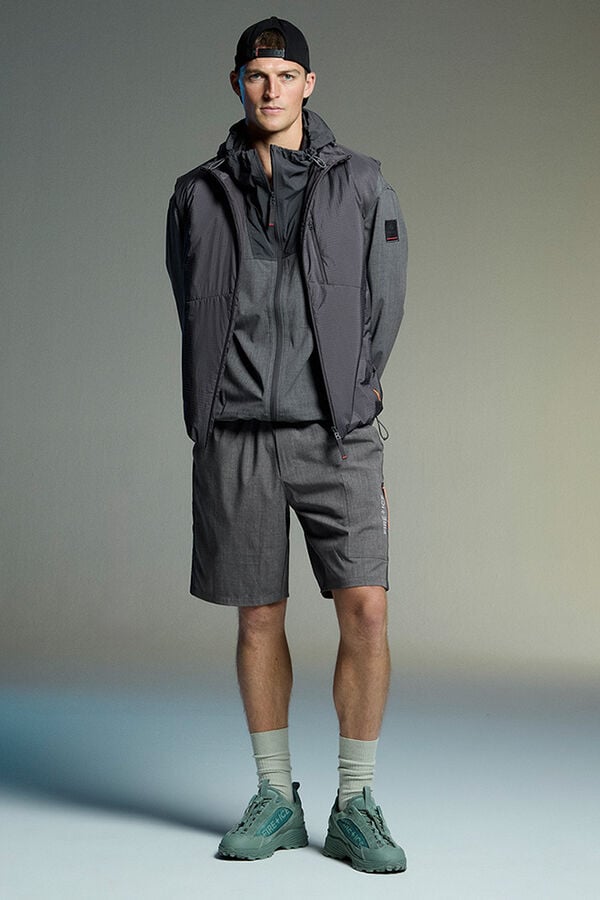 Das Herren Model tr&auml;gt einen Monochrome Look in Grau, bestehend aus leichter Jacke, Weste und Shorts.