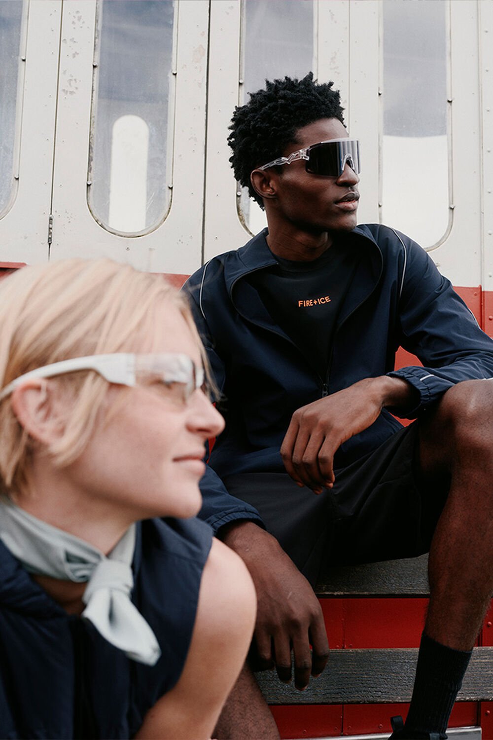 Close-up von zwei Models in sitzender Pose mit Sonnenbrillen. Sie tragen leichte FIRE+ICE Looks in Navy-Blau.