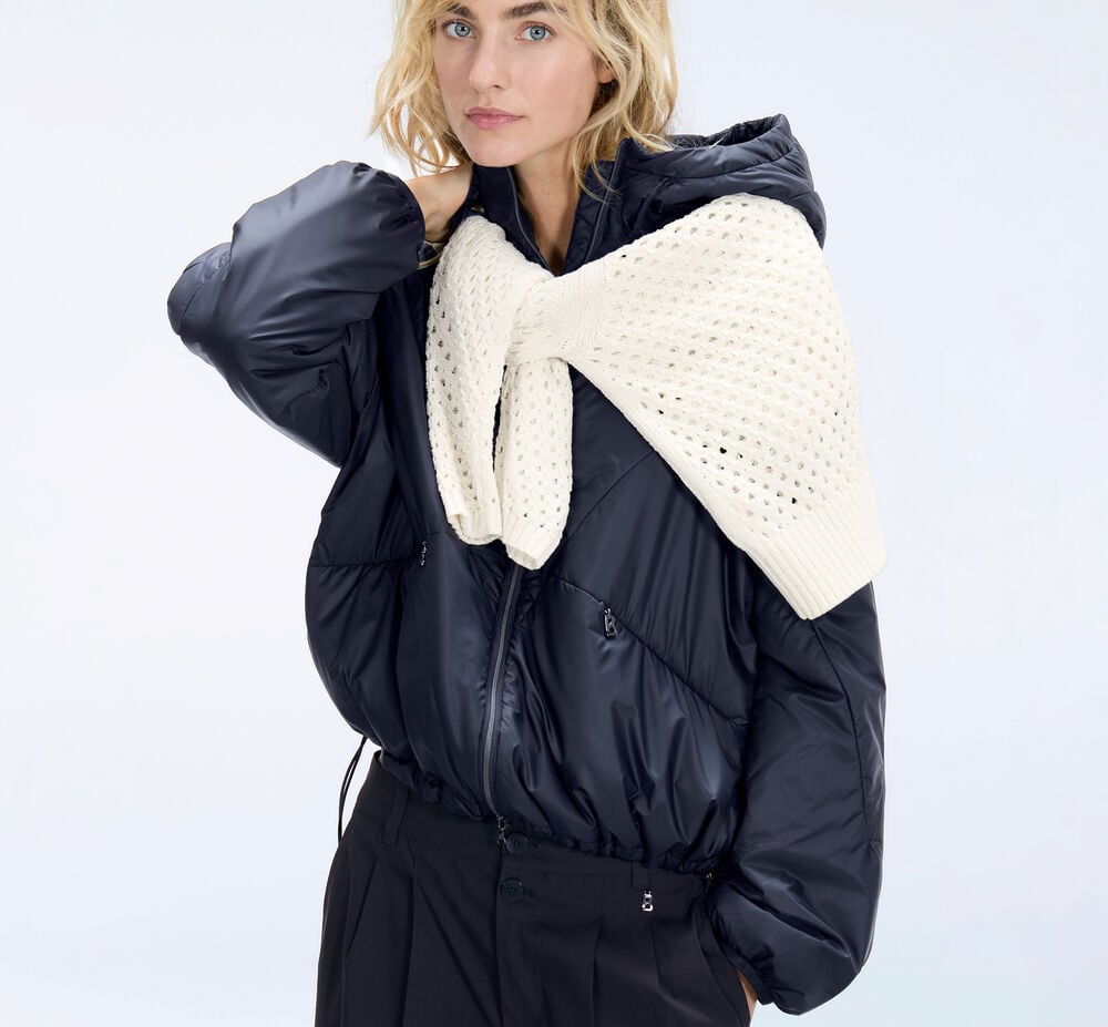 Side view of the female model. She is wearing a navy blue set and carrying a bag and hat made of bast.