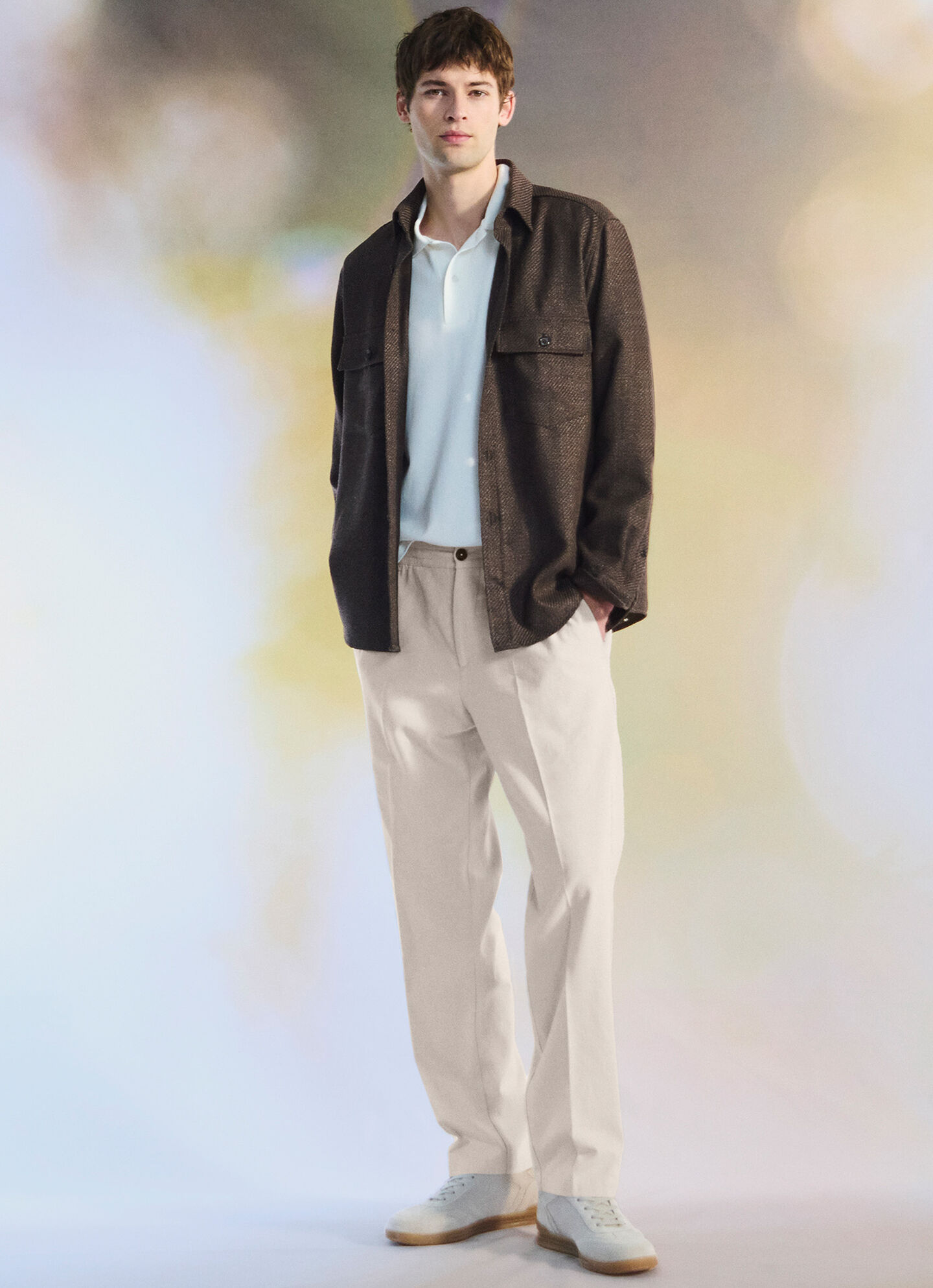 The male model wears a light polo shirt, a dark brown shirt jacket and beige-coloured suit trousers.