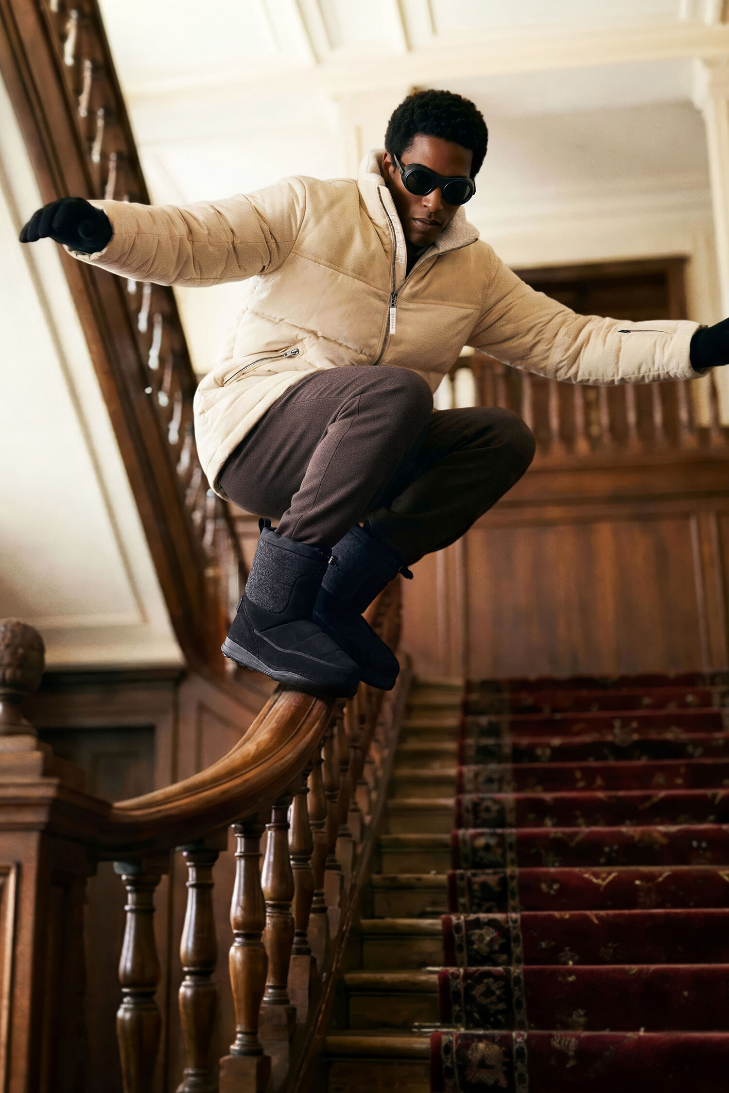 Le mannequin prend une pose dynamique sur la rampe d&rsquo;escalier d&rsquo;un h&ocirc;tel et porte le manteau Mace.