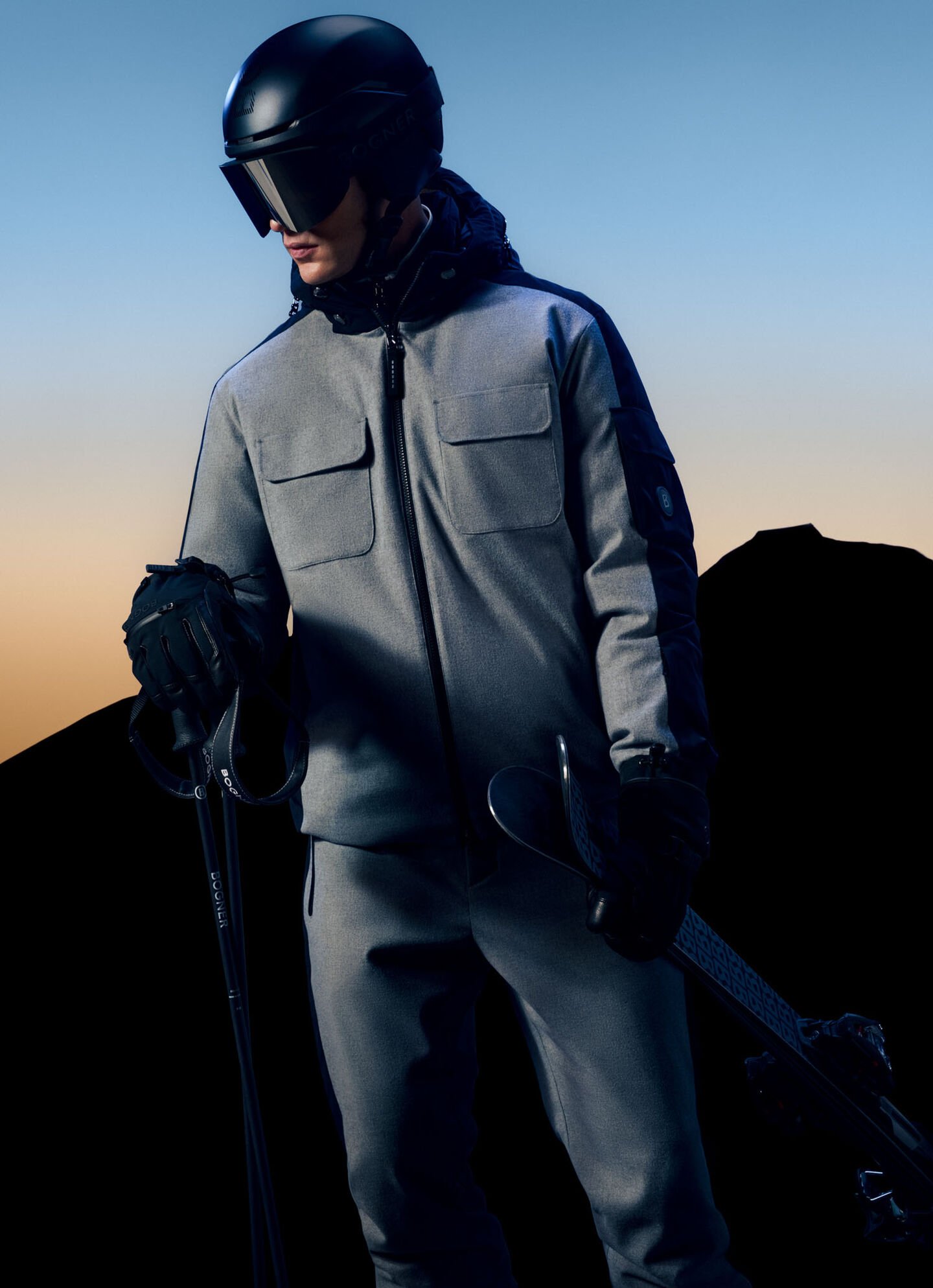 Das Model trägt eine graue Skijacke, graue Skihose, Handschuhe, Skhelm und Skibrille. 