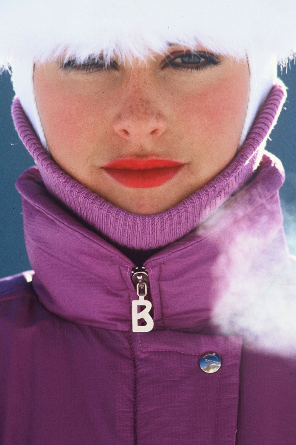 The model is wearing a purple ski jumpsuit featuring the legendary B-zip.