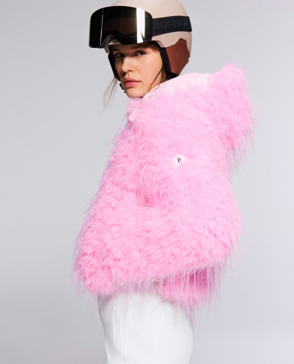 The female model wears the Kela faux-fur ski jacket in vibrant Neon Pink, paired with a ski helmet.