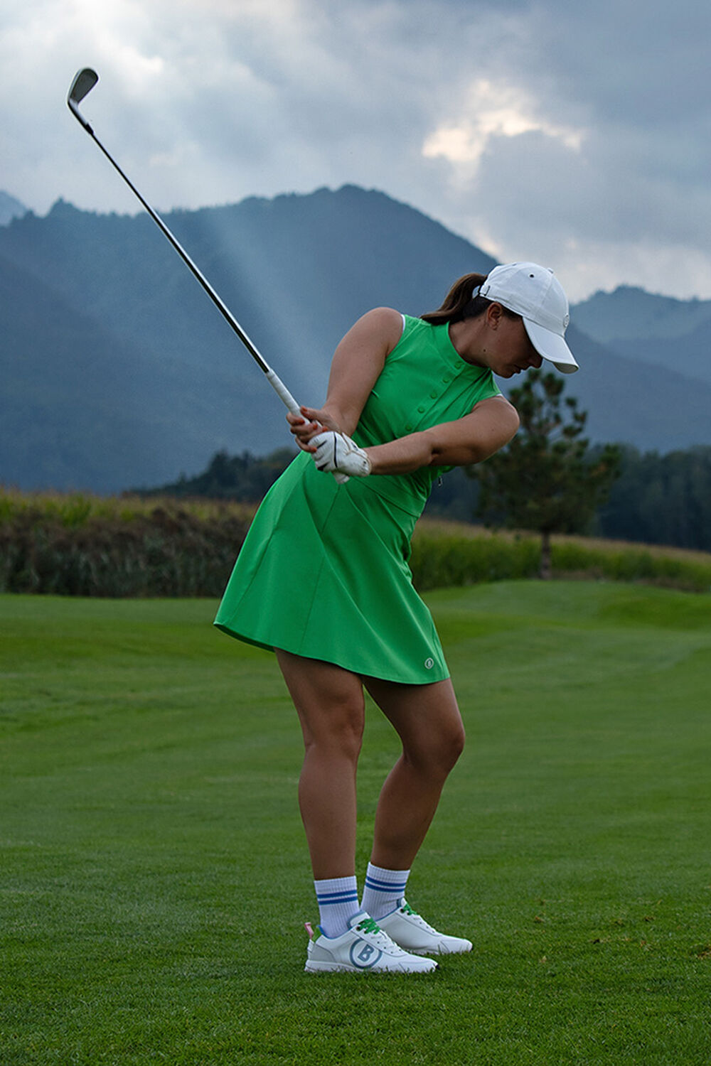 The female golf player is teeing off. She wears a bright green sports dress and golf trainers.