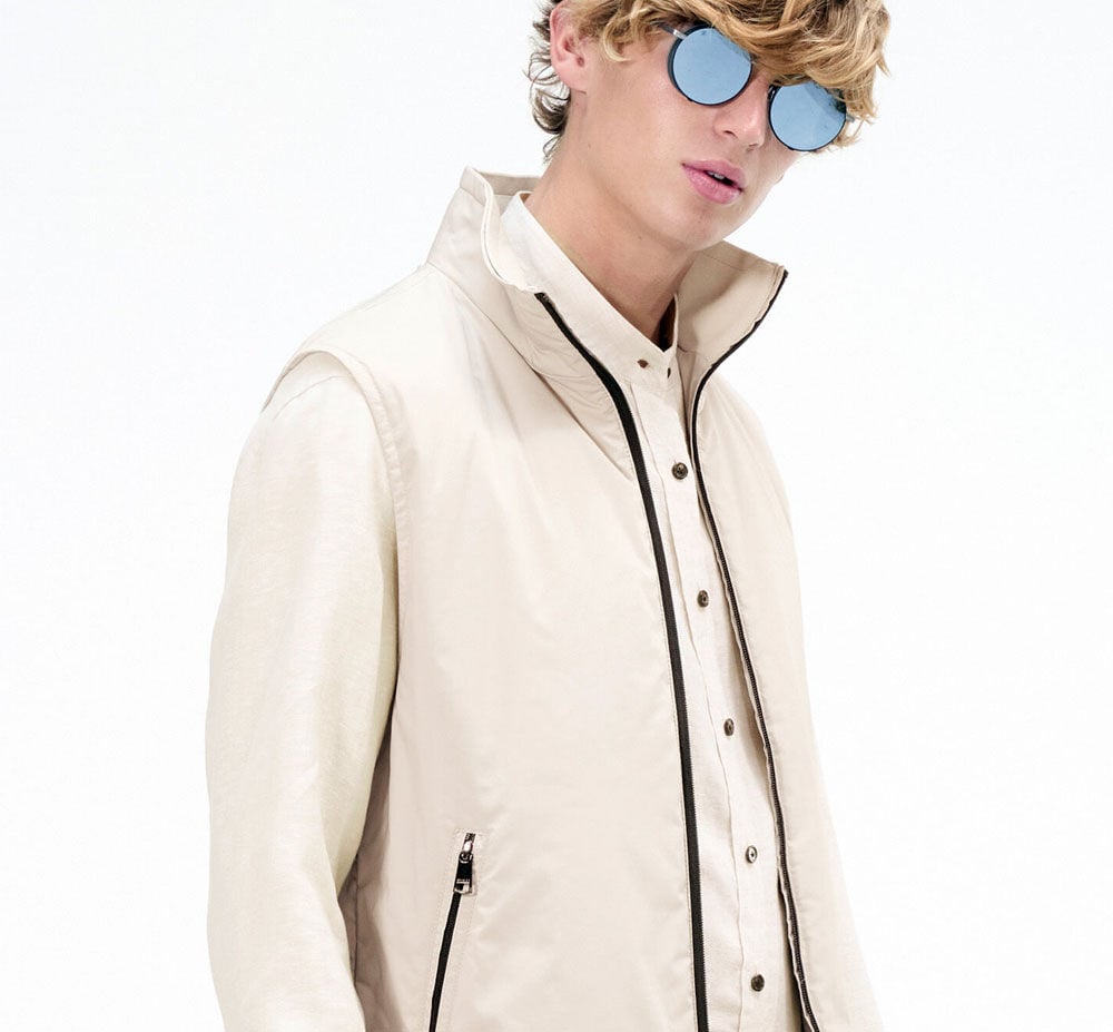 Close-up of the male model in a beige shirt and vest with contrasting black and brown details.