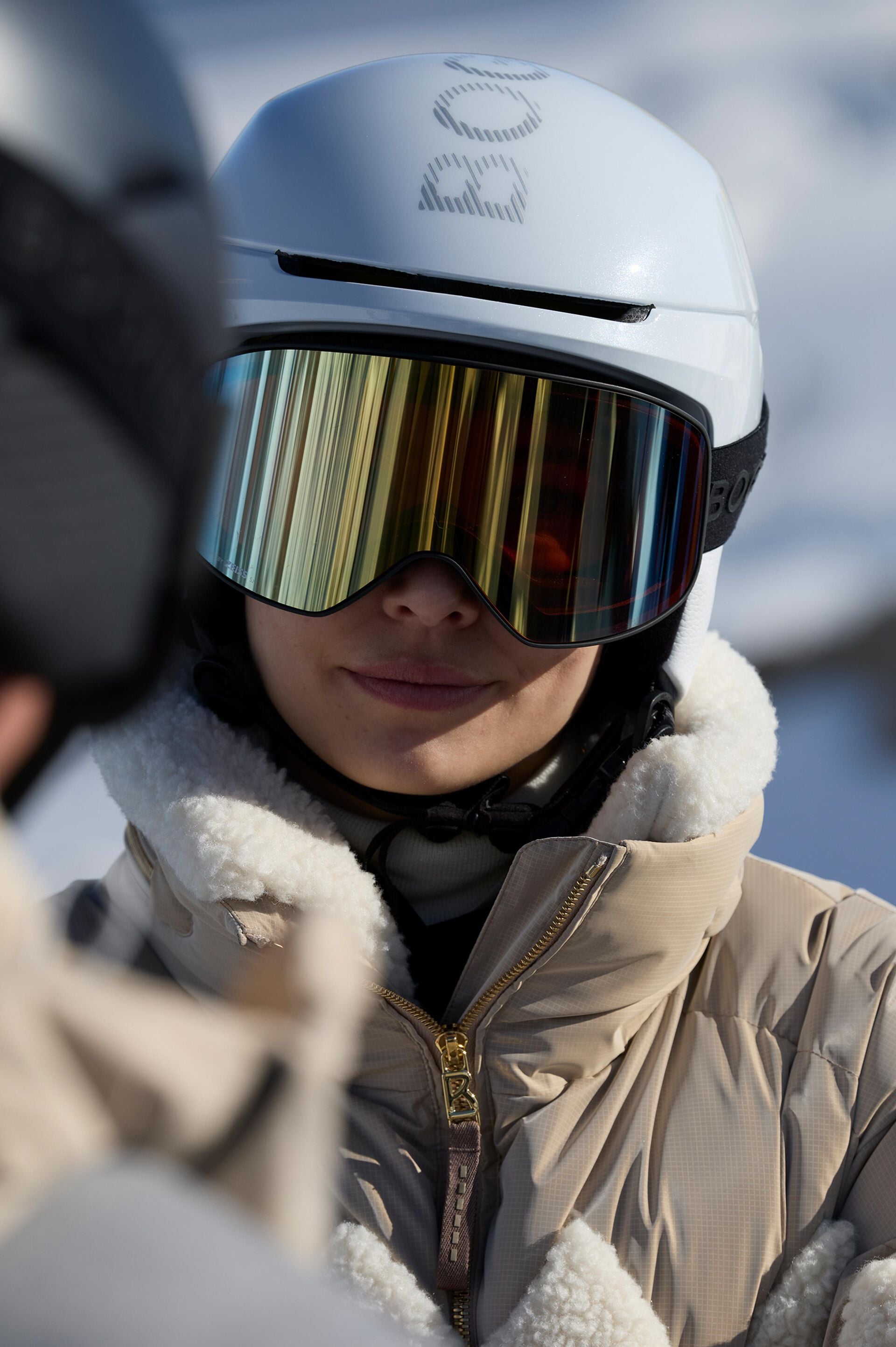 The model is wearing the Minu ski jacket, featuring corduroy panels and teddy fleece details, paired with the Cortina ski helmet.