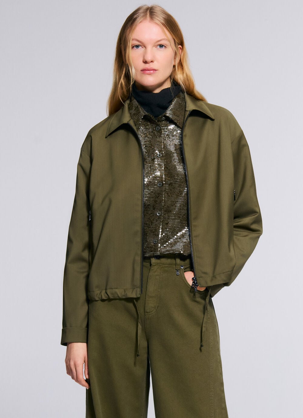 The second female model is wearing a set in pure new wool in olive green, comprising an Elody blouse and Effy trousers.