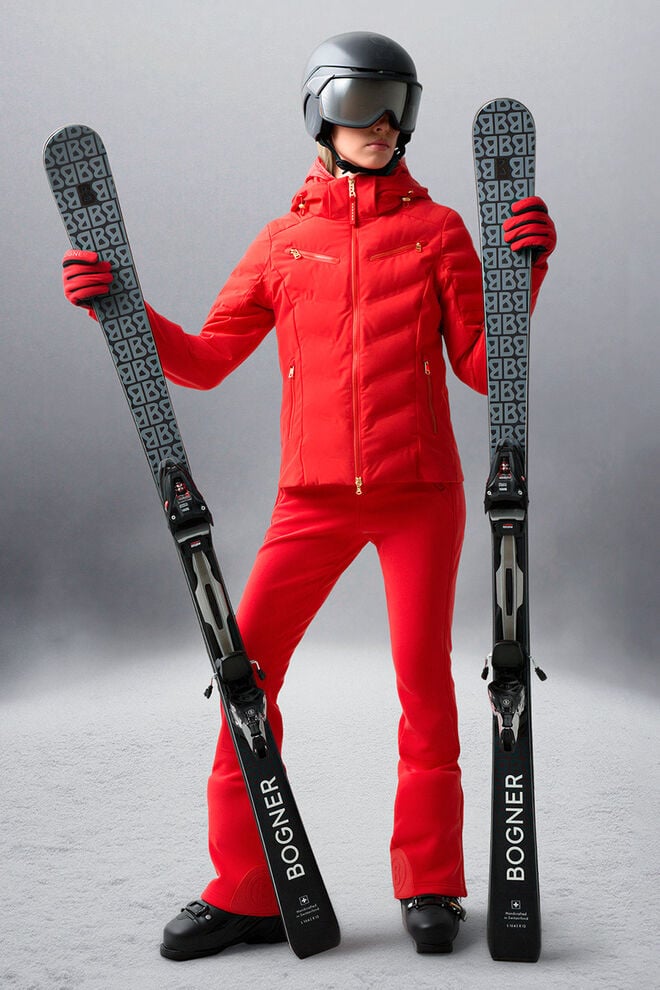 The model is wearing a red ski outfit and holds a pair of skis in her hands.