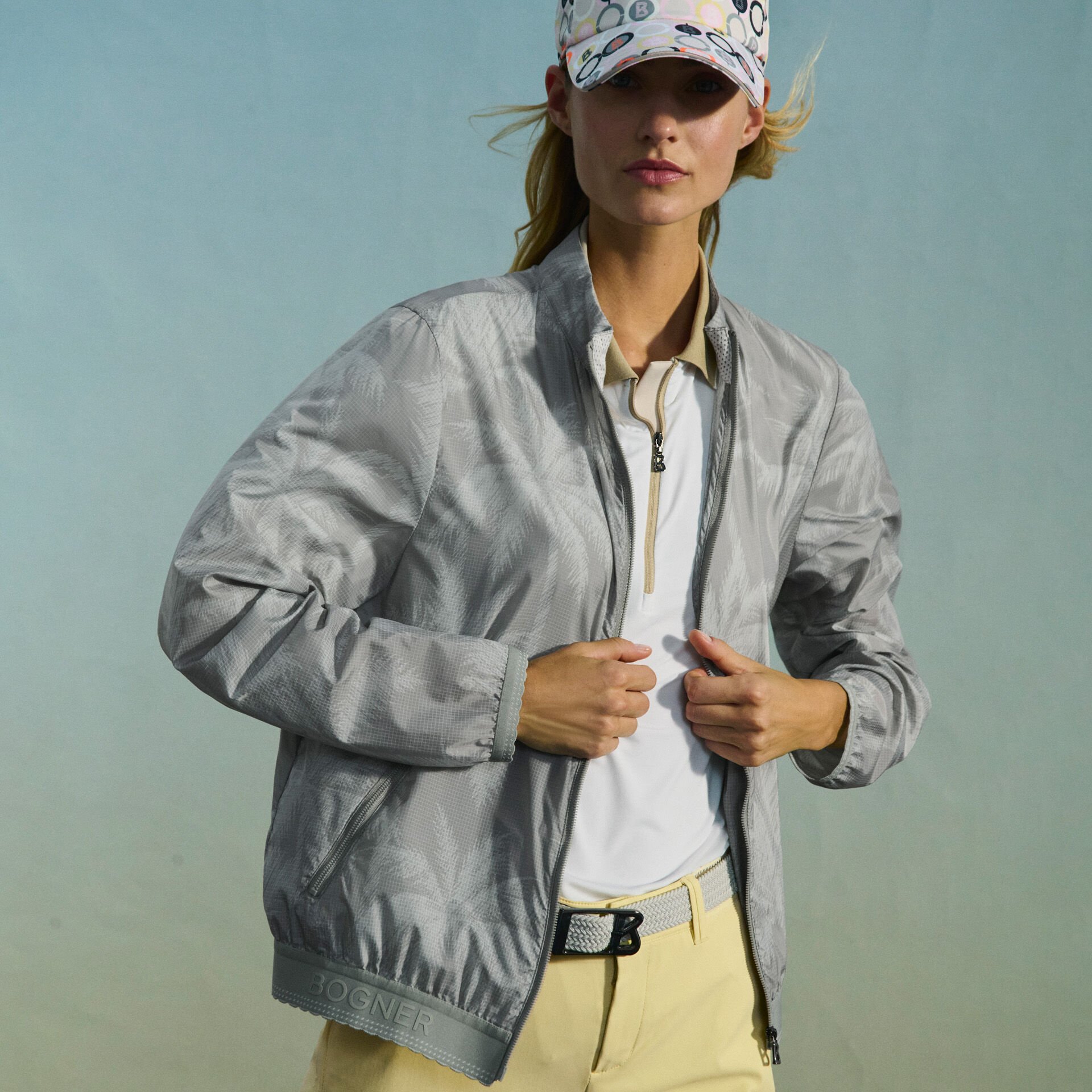 The female model wears a polo shirt and short yellow pants. Her blouson jacket is printed with a palm tree motif.