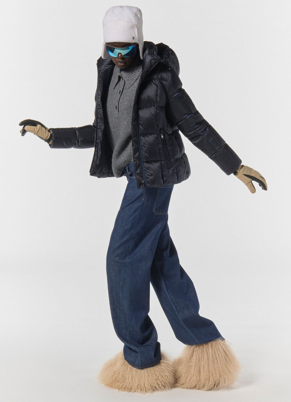 A moving image of a model wearing a cap and sunglasses, dressed in a black down jacket, loose trousers and fur boots.