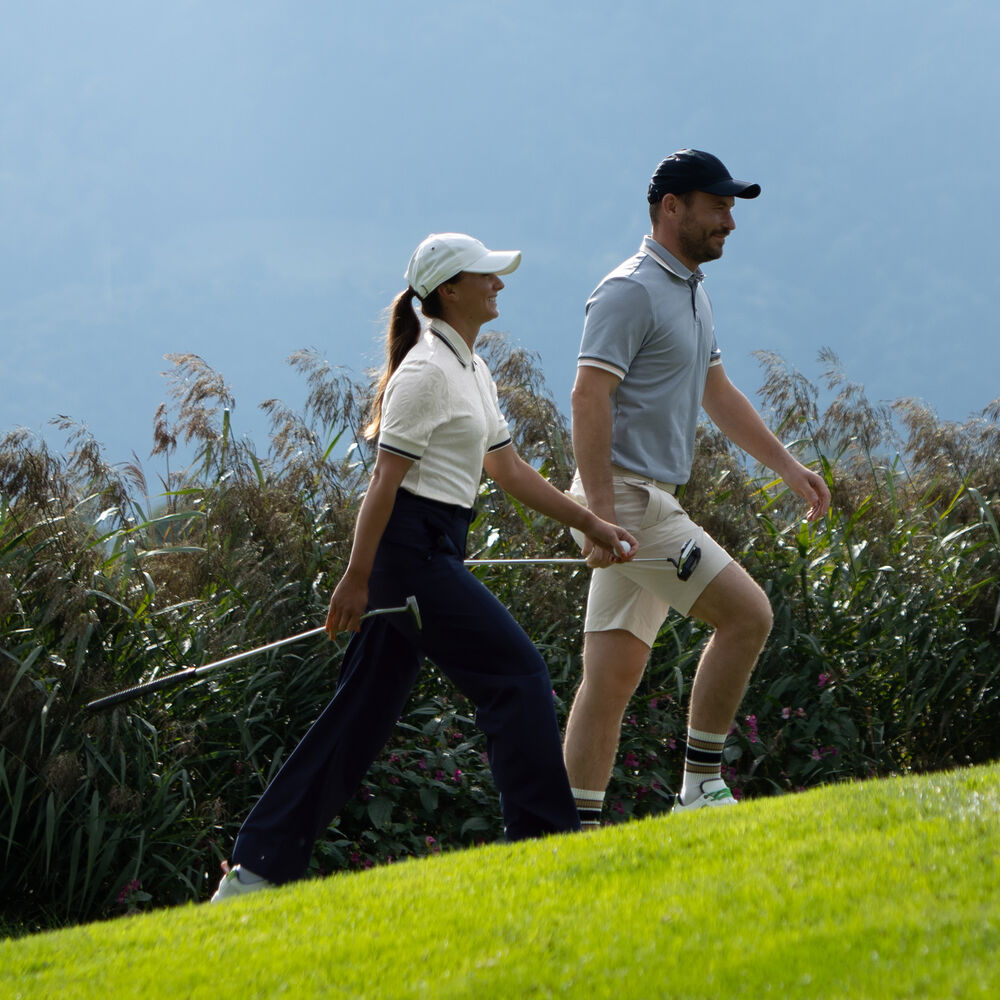 Side view of a female and a male golf player, walking the green and getting ready for tee off.