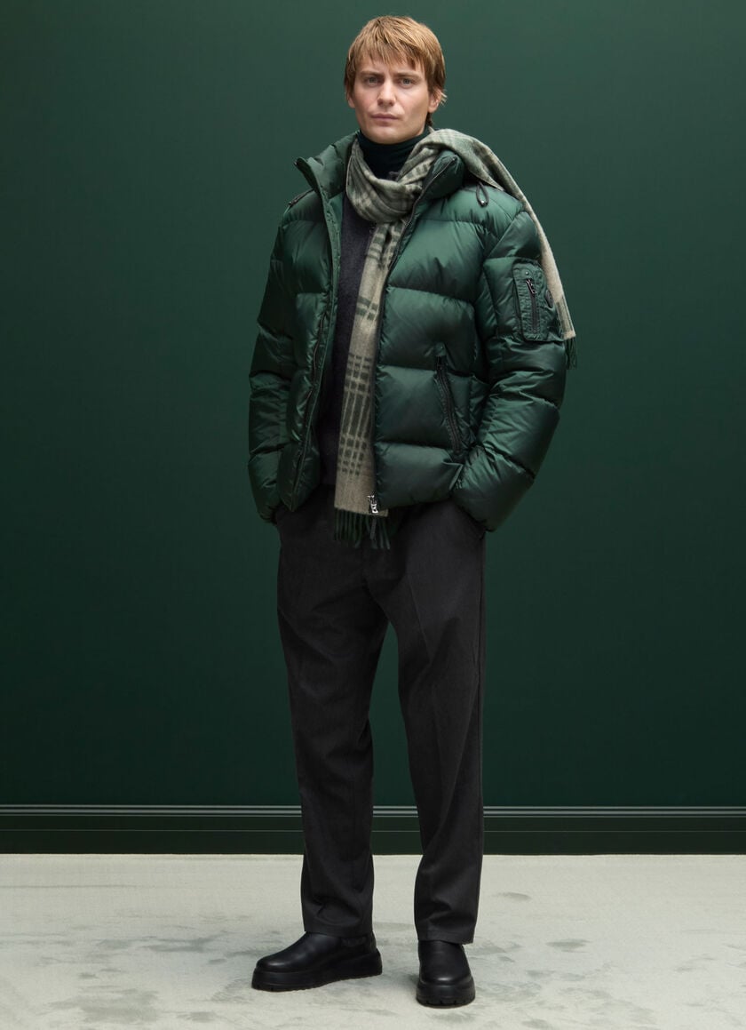 Complete look of the male model – a dark green down jacket worn with a checked wollen scarf and relaxed pants.