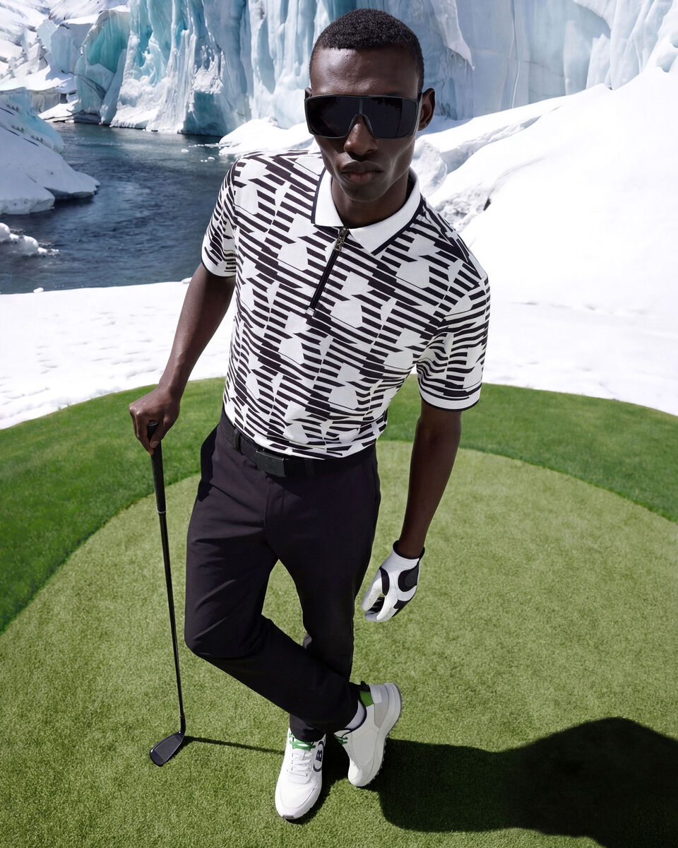 Das Herrenmodel tr&auml;gt ein modernes Golfoutfit bestehend aus einem Poloshirt mit Print und einer sportiv-eleganten langen Hose.