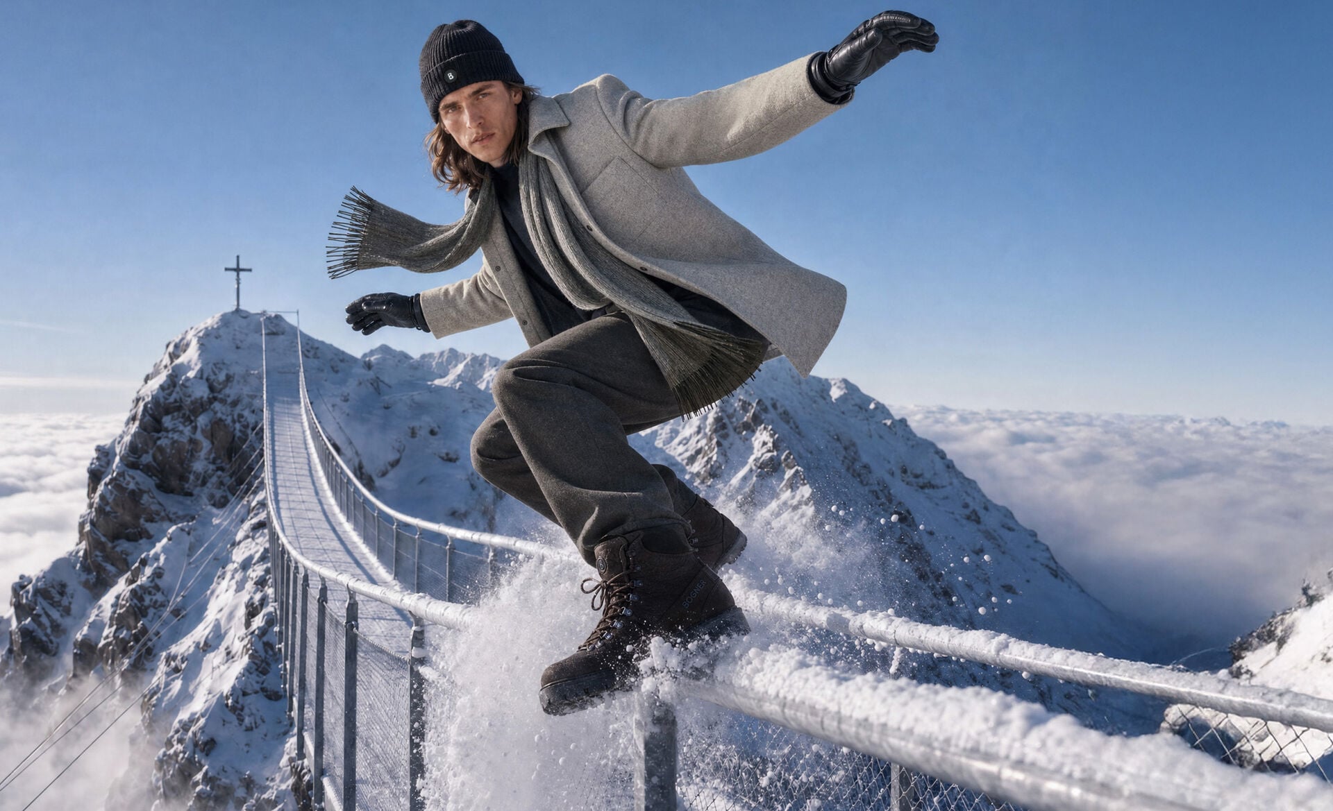 The male model is striking a dynamic pose wearing a light grey shirt jacket, straight trousers and boots. Winter accessories in black and grey complete the look.