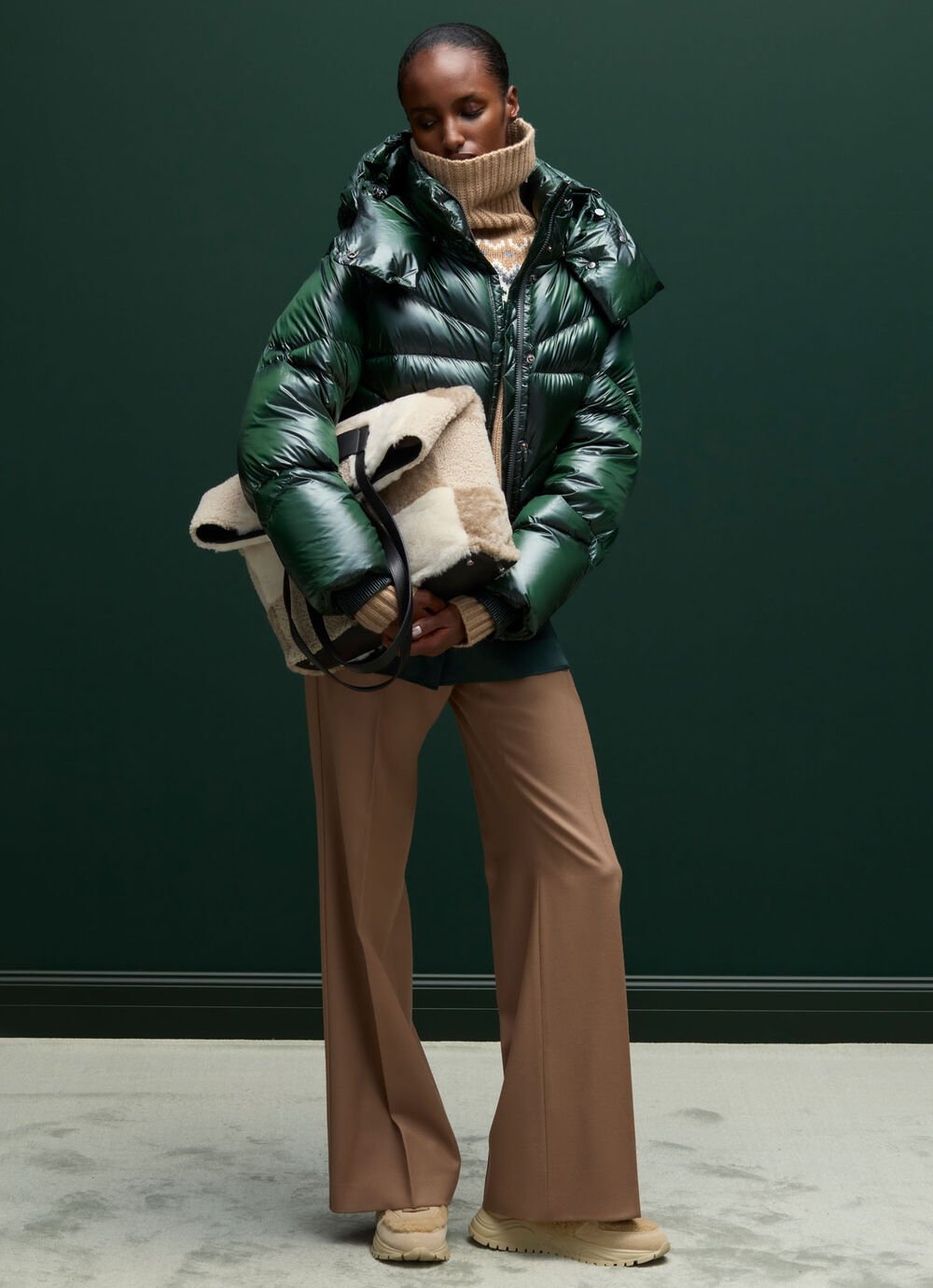 Ce look féminin combine un pull norvégien beige, une doudoune brillante verte et un sac en peau d’agneau.