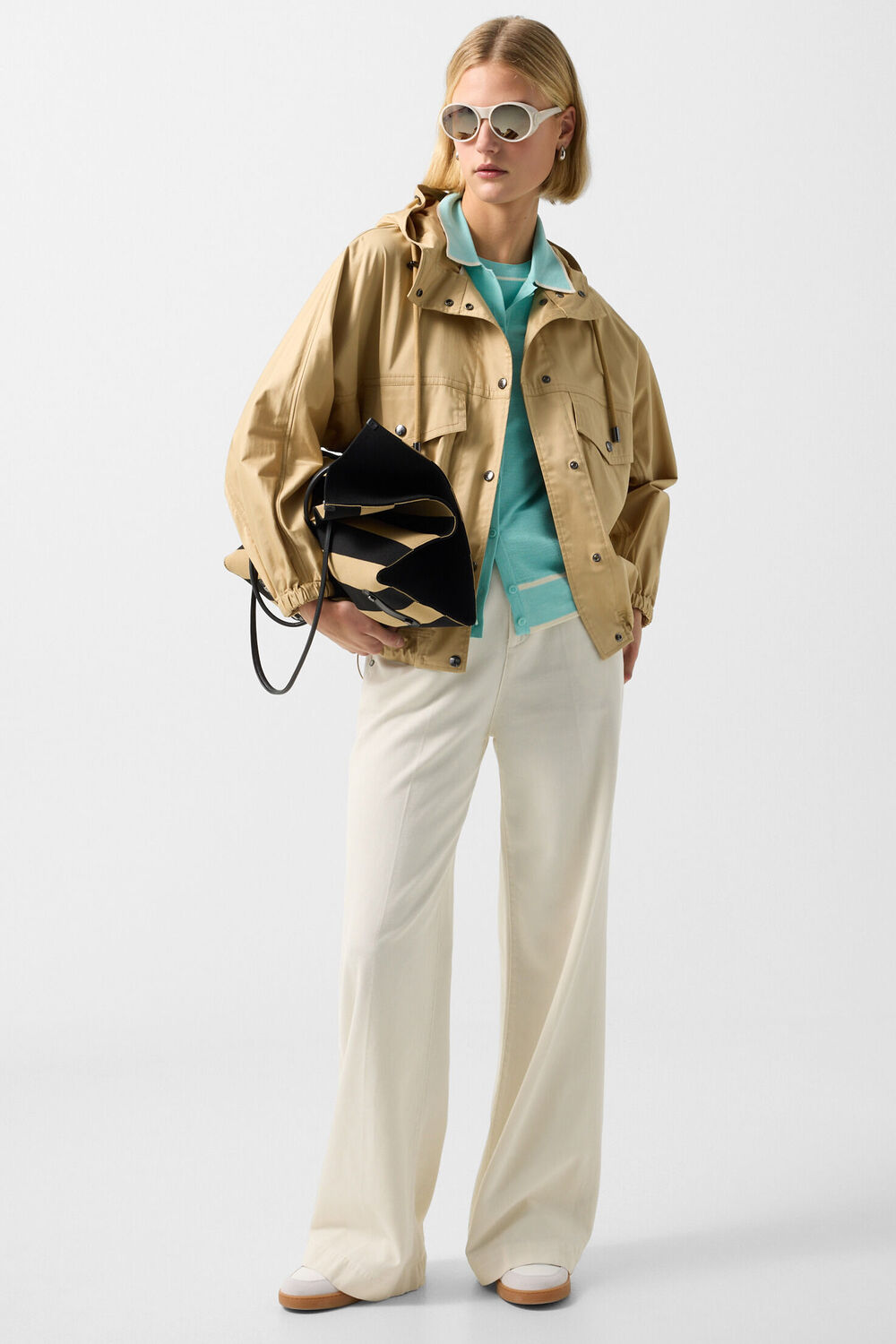 Jacke Noelle in Camel wird am Damen Model mit einem Polo-Shirt in Cyan-Blau sowie einer hellen Hose kombiniert.