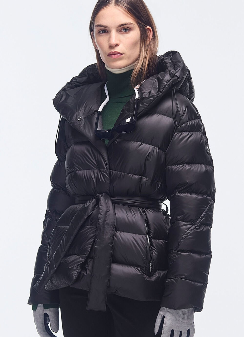A classic: the black hooded down jacket – feminine thanks to the tie belt. Worn with ski gloves and a turtleneck jumper.