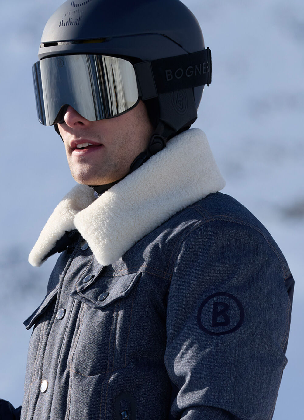 Men's model showcasing the Jeen denim ski jacket with a contrasting fur collar and satin back panel. A "B" logo embroidery on the sleeve completes the design.