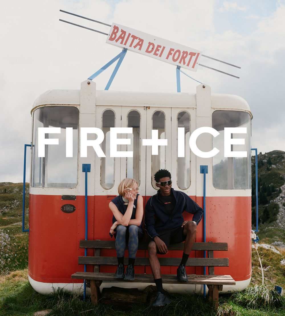 Photograph of a red ski gondola on the mountain with a sportswear-clad female and male model sitting on a bench in the foreground.