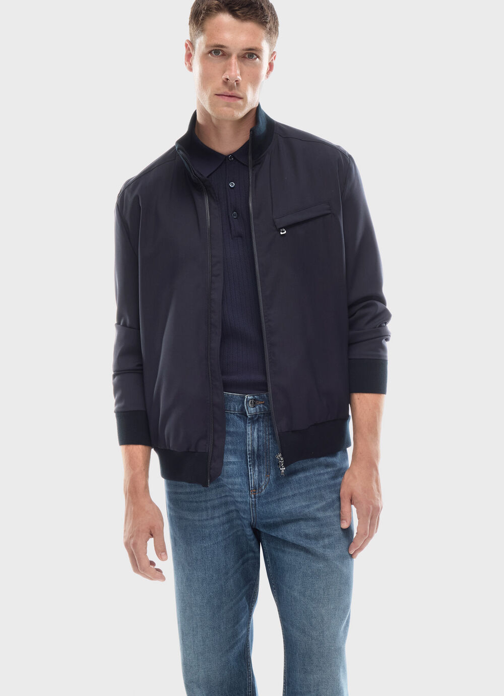 Das Model tr&auml;gt eine dunkle Blousonjacke, darunter ein navy-blaues Polo-Shirt und relaxte Jeans.