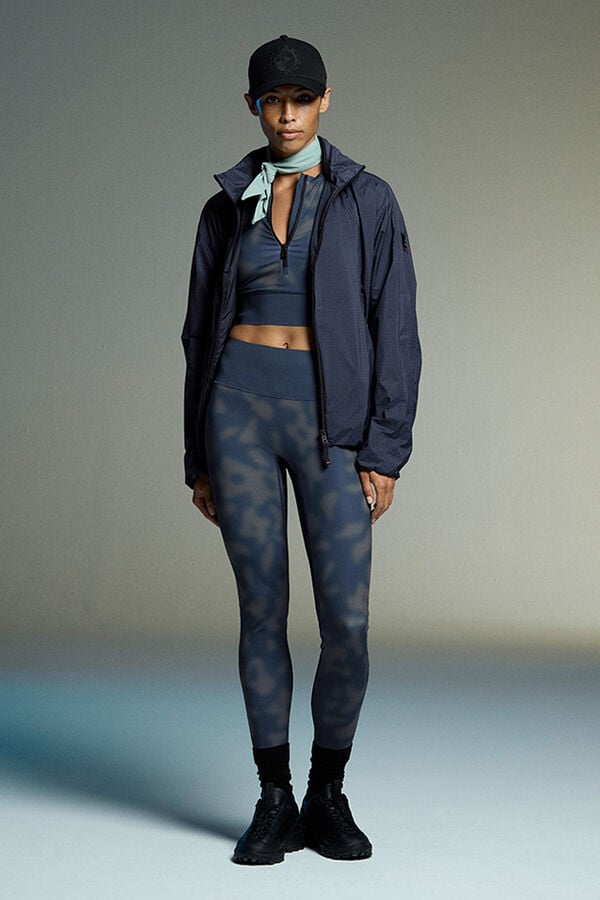 Das Damen Model tr&auml;gt ein Yoga-Set mit grafischem Print, bestehend aus Top, Tights und leichter Jacke.