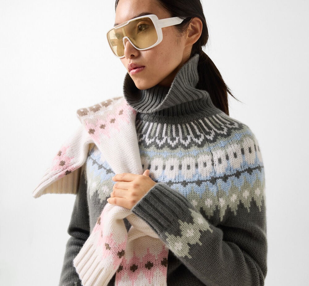 Das Damen Model tr&auml;gt den gr&uuml;nen Pullover Ingrid mit labeltypischem Norwegermuster in elegantem Wei&szlig;, Blau und Hellgr&uuml;n, dazu eine wei&szlig;e Sonnenbrille mit hellen Gl&auml;sern.