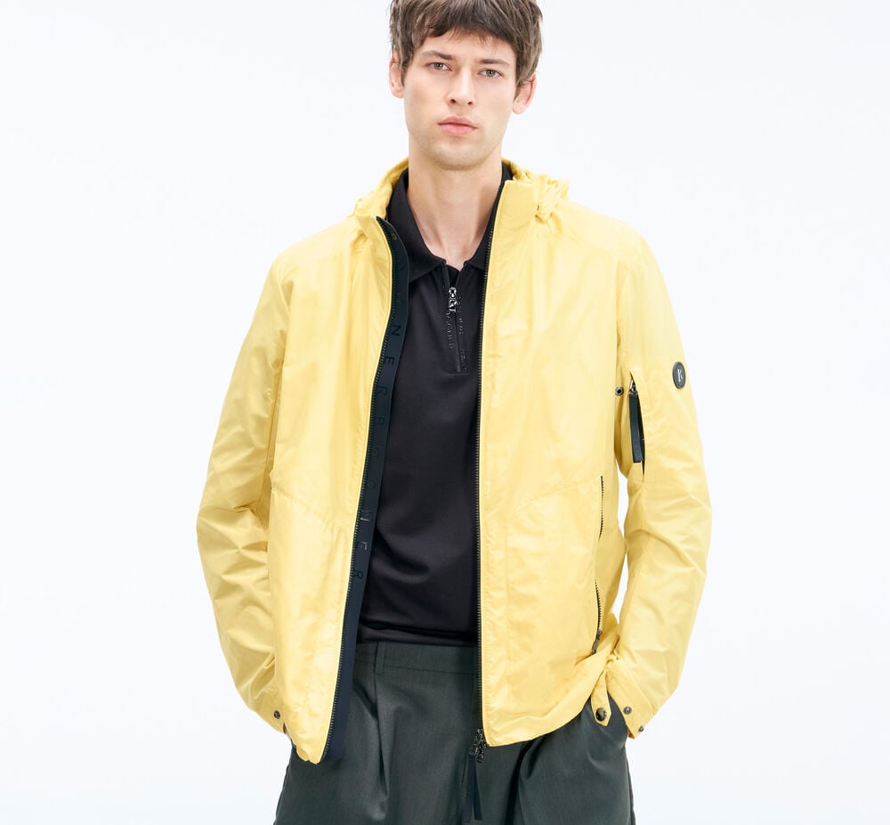 Das Herren Model tr&auml;gt Blouson Jacob in Sonnengelb, dazu ein schwarzes Polo-Shirt und Shorts.