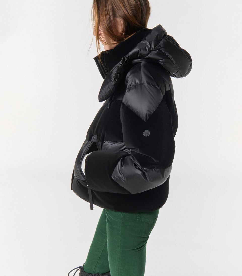 Side view of a V-quilted down jacket in a multi-material design in black combined with green trousers. Side view of a V-quilted down jacket in a multi-material design in black combined with green trousers.