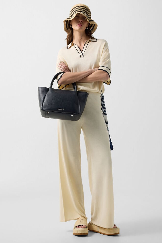 Das Damen Model tr&auml;gt Strick-Polo-Shirt Paris und Strickhose Paula in Creme, dazu einen Basthut und eine Tasche.