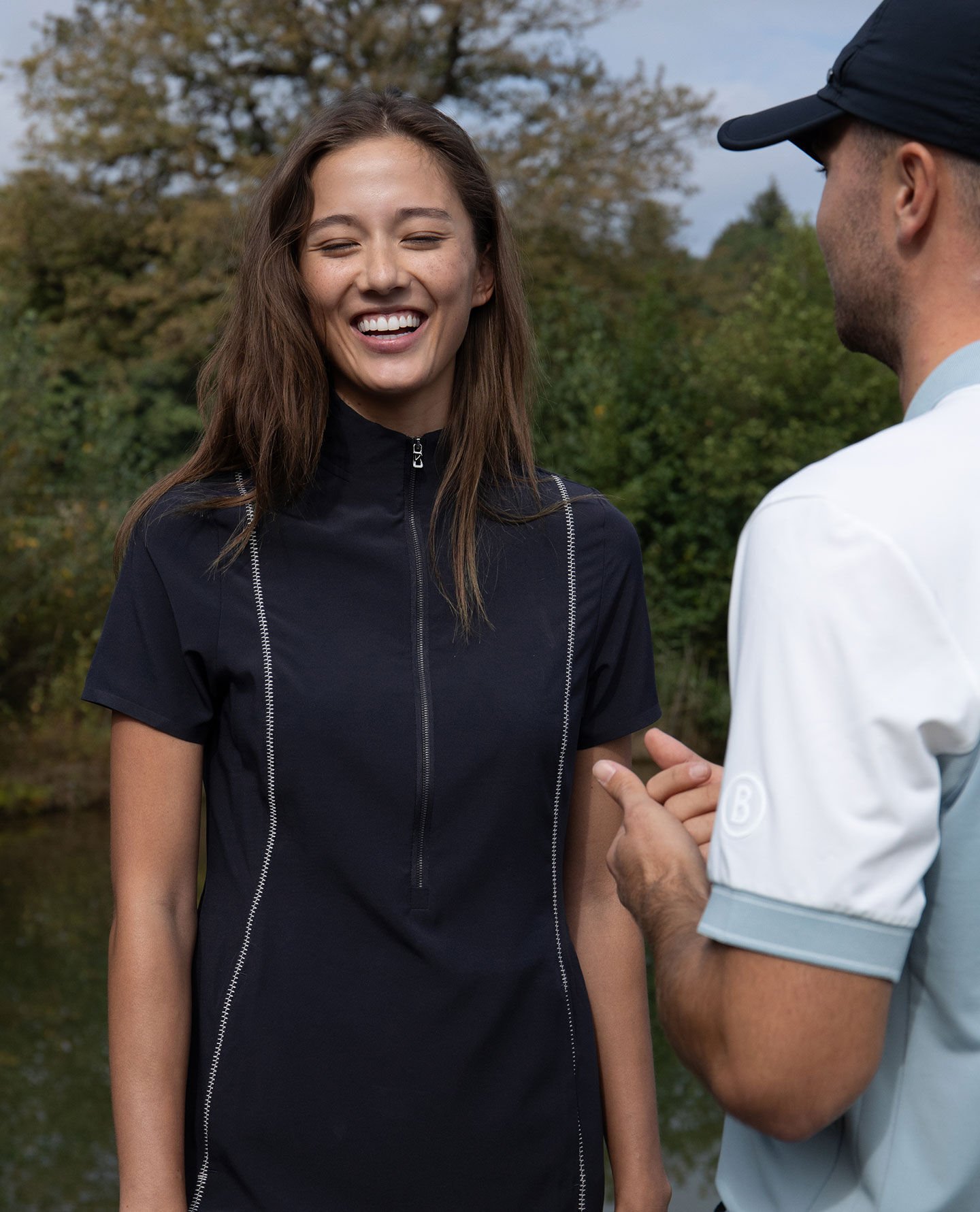 Half-body shot of a female golfer wearing a dark blue golf dress. She has her eyes closed and is smiling.