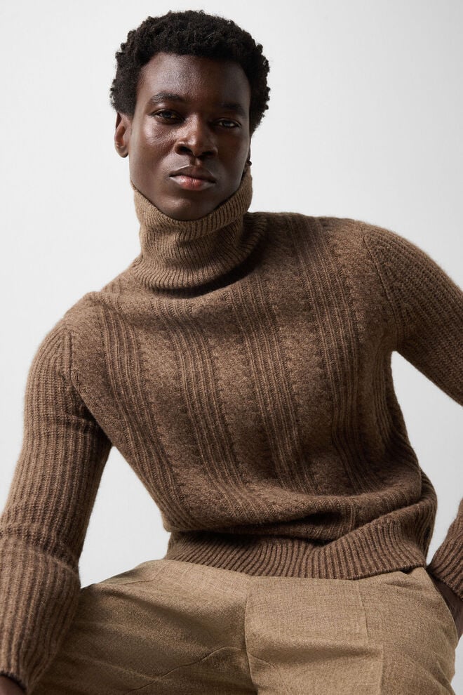 The male model is wearing the Eros sweater in yak wool with a high collar and tonal pattern.