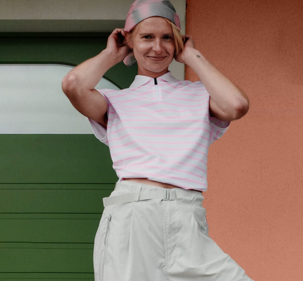 The female model is wearing a polo shirt in pink stripes and the Charis functional trousers.