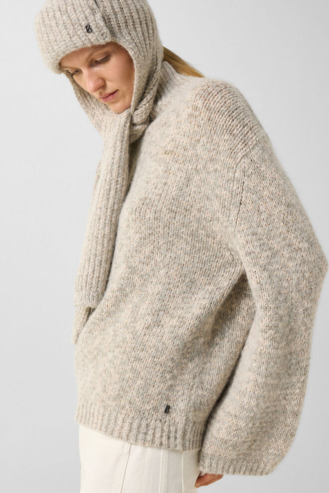 Das seitlich stehende Model tr&auml;gt den Svoni Pullover mit hohem Kragen sowie die edle Schalm&uuml;tze Suzanne.