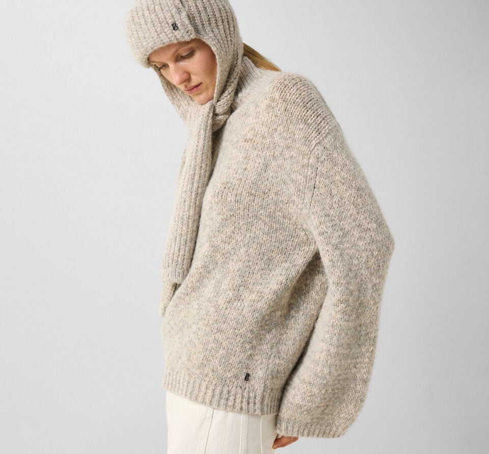 The model standing to one side is wearing the Svoni pullover with a high collar and an elegant Suzanne balaclava.