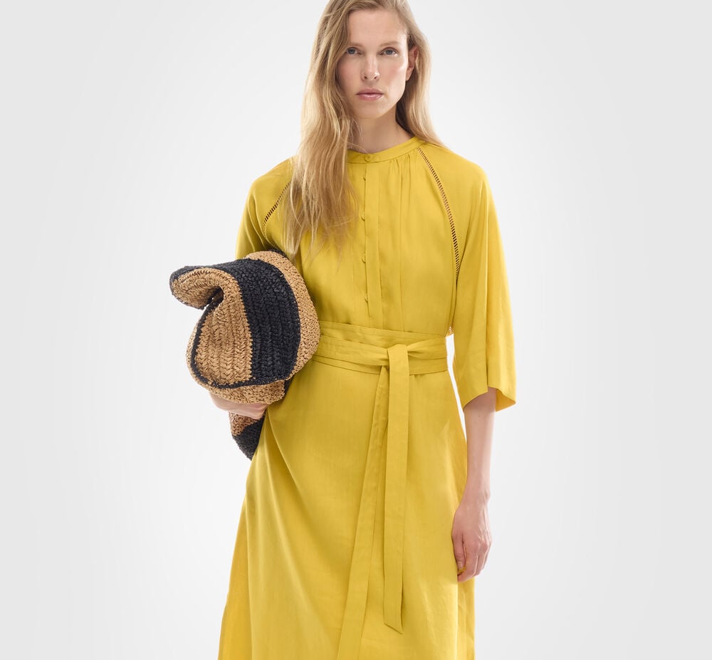 Das blonde Damen Model tr&auml;gt ein luftiges langes Kleid in Sonnengelb mit Broderie Anglaise Details.