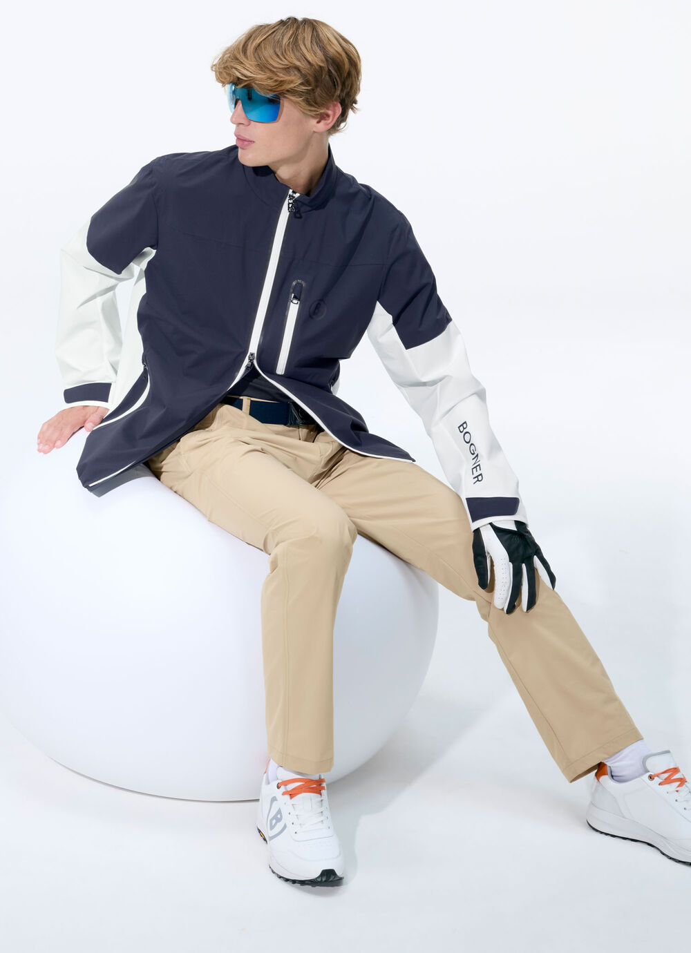 The male model wears a lightweight blouson jacket in dark blue and white, combined with long beige pants.