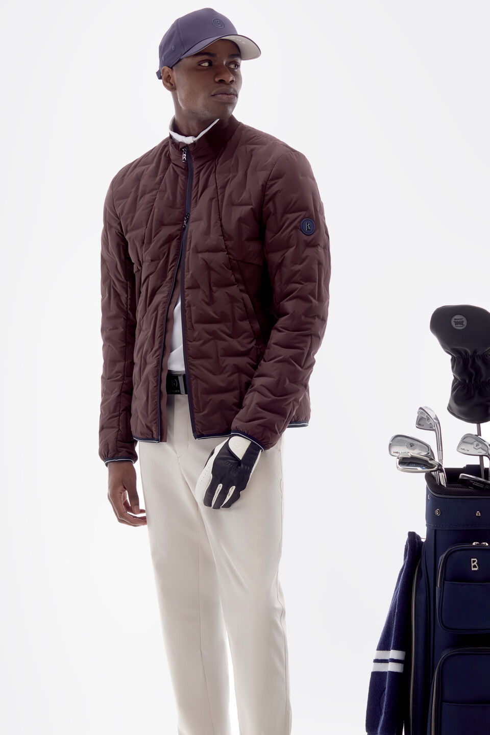 The model is wearing a wine-red lightweight down jacket from the Golf Collection, a cap and a pair of white golfing pants.