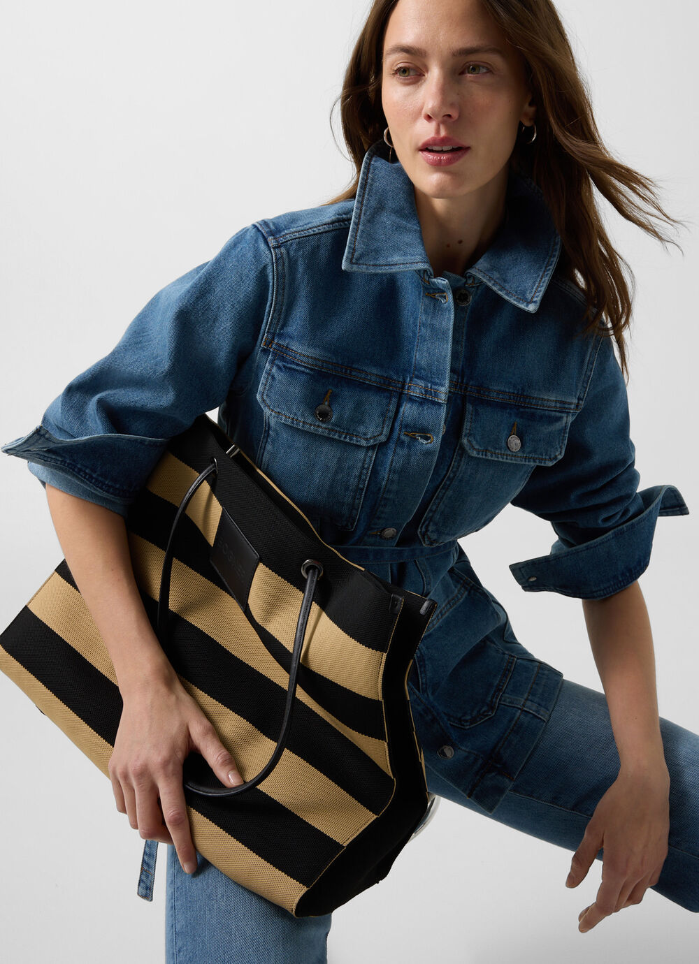 The female model in a full denim look carries a big shopper made from natural fibres with a bold striped pattern in beige and black.