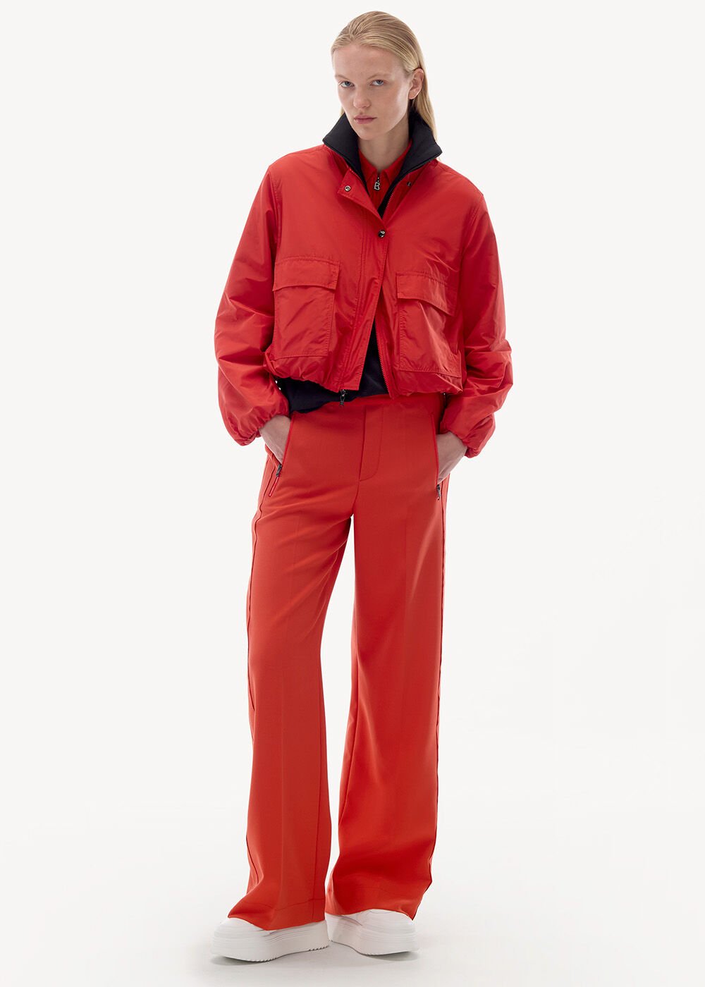 The model is wearing a cropped jacket in red with matching red trousers – paired with white platform trainers.
