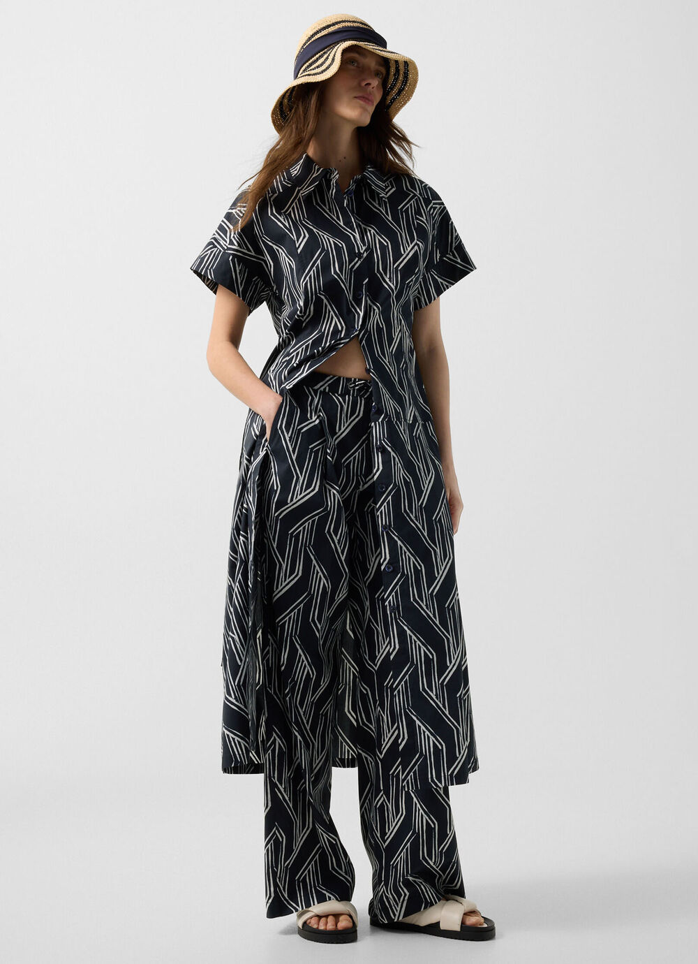 The model is wearing the Roxana shirt dress with graphic print, paired with the matching Gina long trousers.