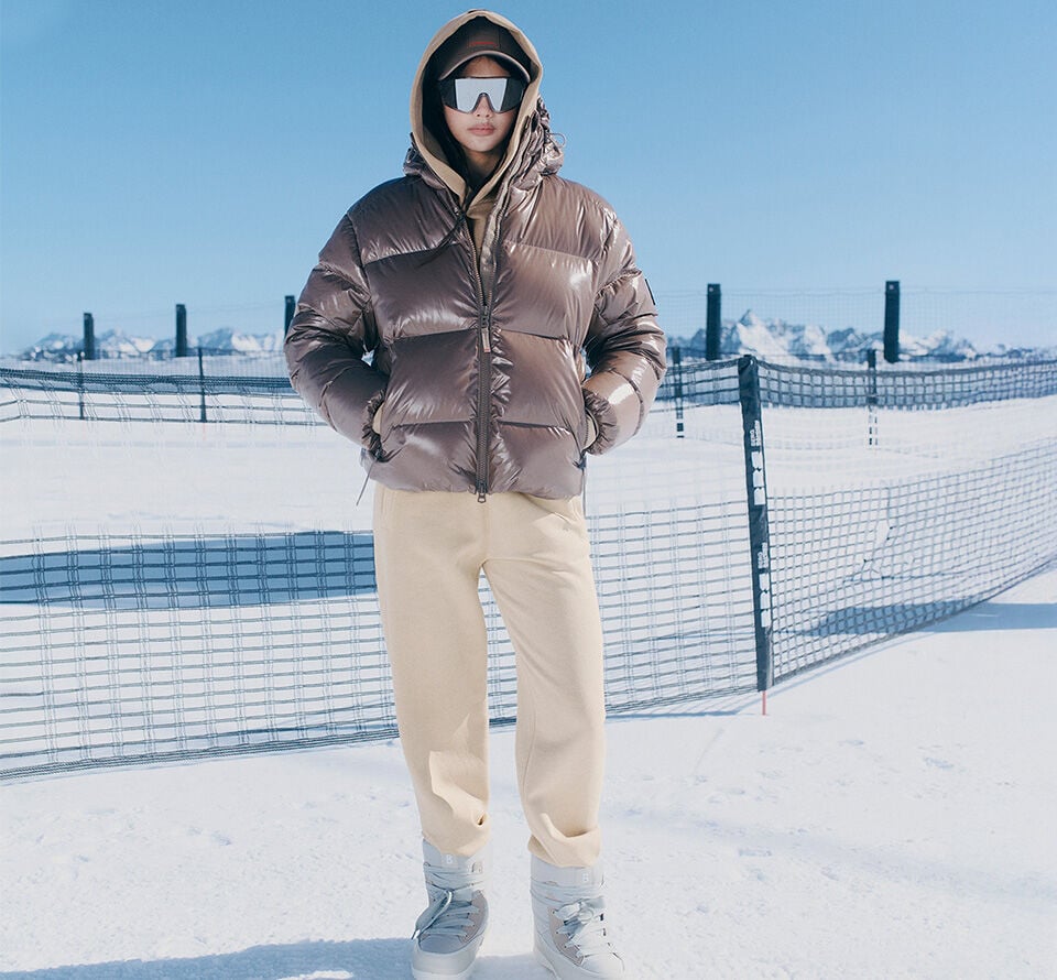 The female model is wearing a shiny short down jacket in the snow.