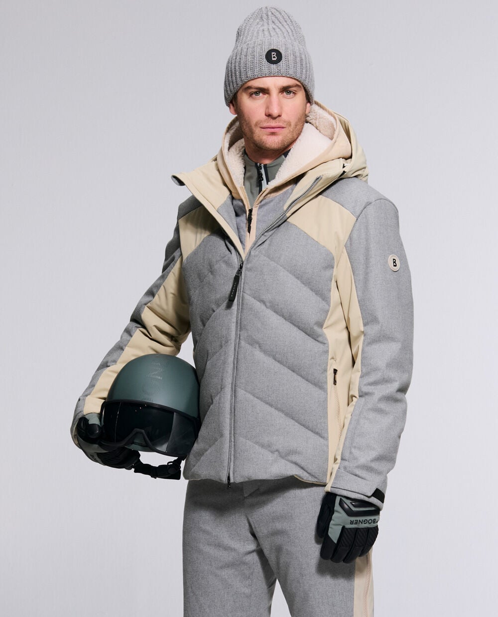 Le mannequin homme porte la veste de ski Flann en flanelle gris clair et beige avec le pantalon de ski Firat et le bonnet Bony.