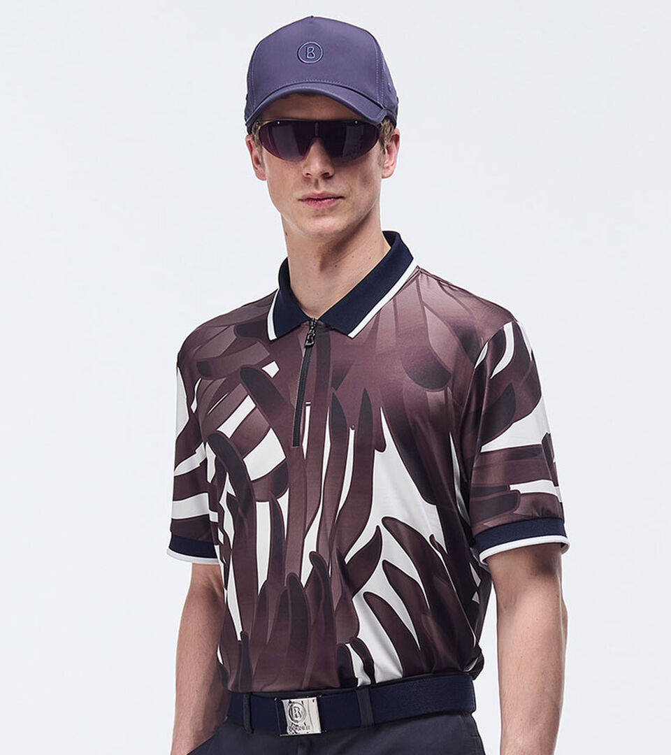 Das Herrenmodel präsentiert sich mit einem weinrot-weißen Polo-Shirt mit auffallendem grafischem Print. 
